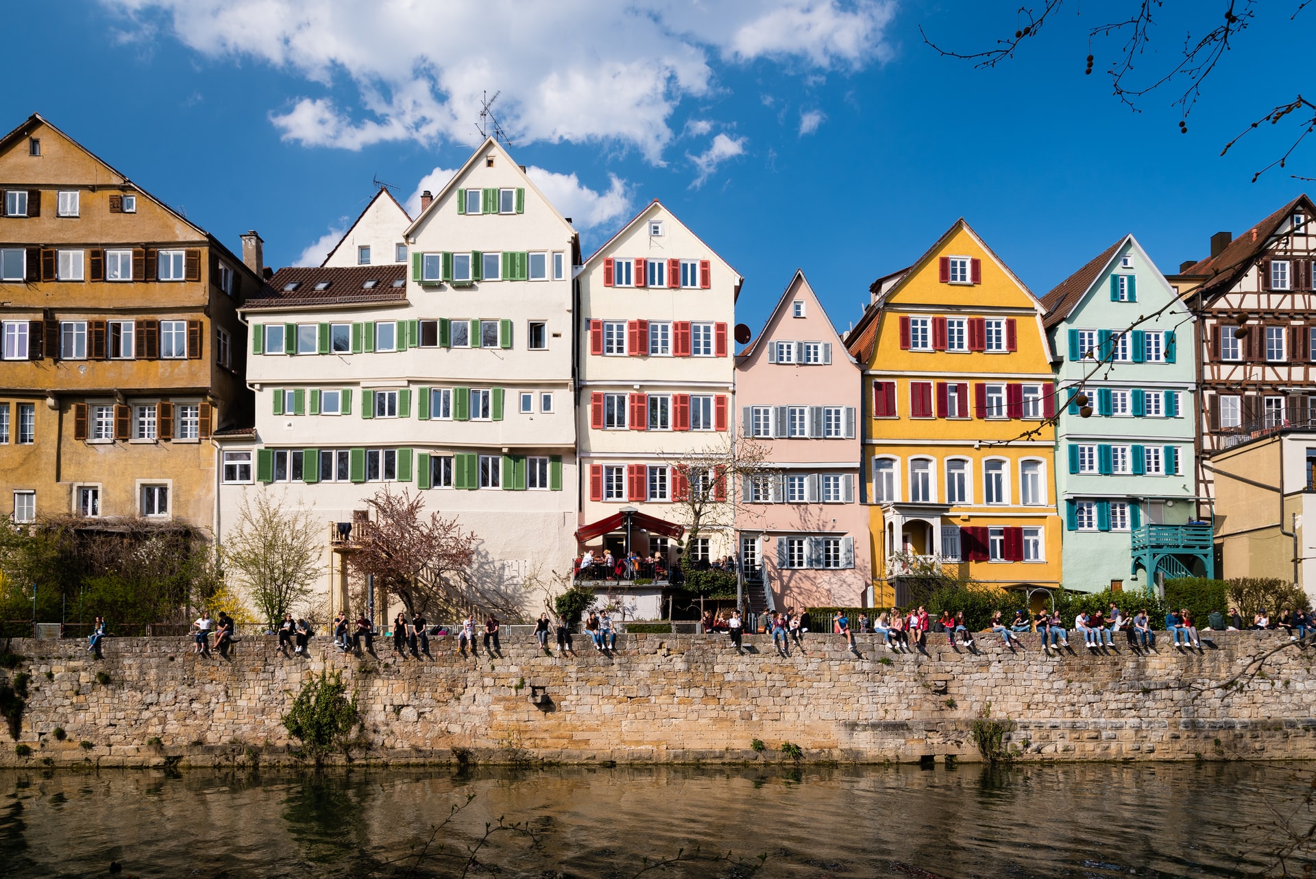 Colourful houses at the river. People are sitting on the wall enjoying the sun.